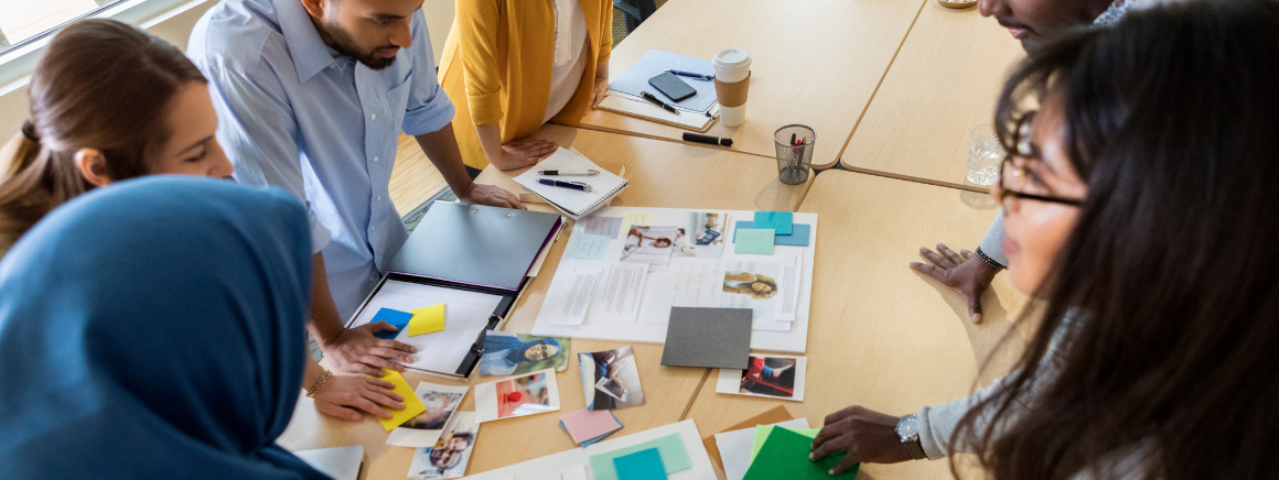 A vibrant brainstorming session with a diverse group of people gathered around a table filled with marketing materials, notes, and digital devices. This image captures the collaborative spirit of crafting a nonprofit marketing plan.